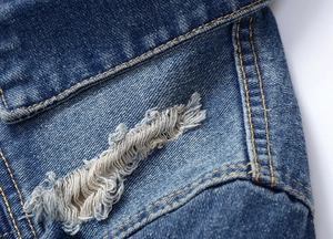 Close-up of blue denim jacket fabric with distressed ripped detail and yellow stitching