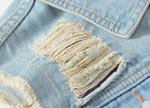 Detailed close-up of light blue denim vest with ripped fabric and metal button