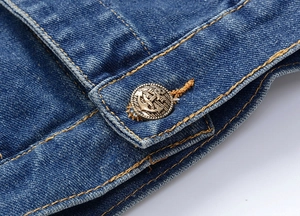Detail of blue denim jacket showing a vintage metal anchor button and orange stitching
