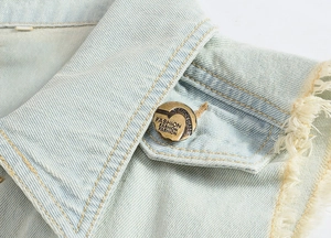 Macro detail of light blue denim vest showing frayed edges and embossed metal button