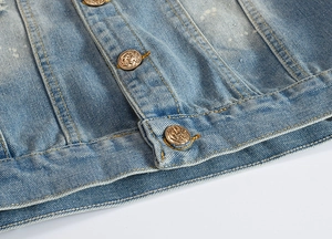 Detailed close-up of light blue washed denim jacket with embossed bronze buttons and ink spots