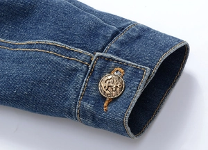 Macro shot of denim jacket cuff with contrast stitching and bronze anchor button
