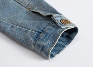 Macro shot of light blue denim sleeve cuff featuring a vintage anchor-etched metal button