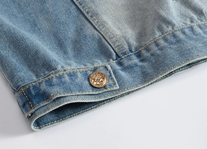 Close-up of light blue denim jacket hem with yellow stitching and anchor metal button
