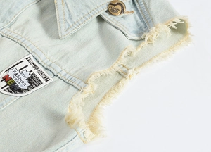 Detail of light blue denim vest showing vintage patches and frayed edge texture
