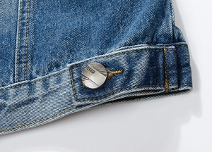 Macro shot of blue denim vest hem showing contrast stitching and metal JEANS button