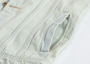Detailed close-up of side pocket stitching and vintage metal button on light blue denim vest