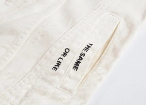 Close-up of cream denim vest featuring black printed text on pocket and twill texture