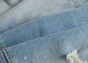 Macro shot of light blue distressed denim fabric with white paint splatters and yellow stitching