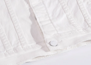 Macro shot of white denim jacket featuring twin-needle stitching and engraved jeans button