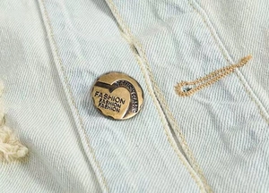 Detail of vintage copper button and yellow stitching on light blue denim vest