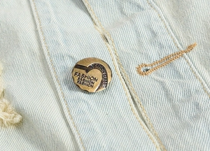Close-up of vintage metal button and yellow stitching on light blue denim vest detail