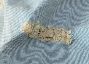 Macro view of light blue denim fabric texture with distressed ripped hole details