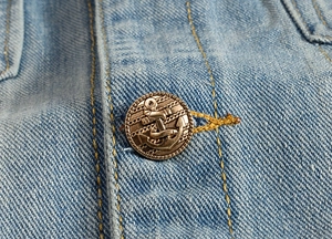 Macro shot of vintage bronze anchor button on light blue denim jacket with detailed relief