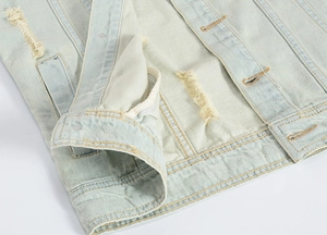 Macro view of distressed light blue denim vest with ripped details and sturdy stitching