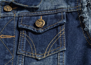 Macro view of blue denim vest with heart-engraved fashion metal buttons and yellow stitching
