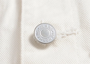 Detailed macro view of a silver metal button with engraving on white denim vest fabric