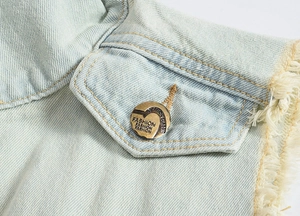 Detail of light blue washed denim vest showing frayed edge pocket and vintage metal button