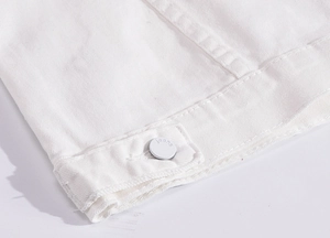 Macro shot of white denim jacket hem with metallic buttons and detailed stitching