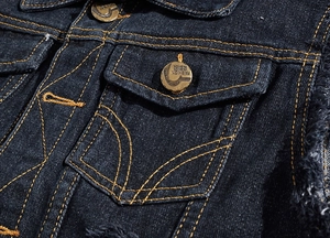Macro detail of dark denim fabric with orange stitching and vintage fashion buttons