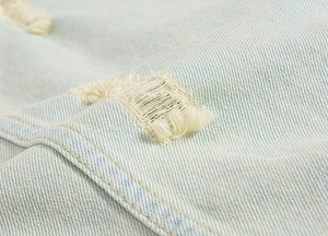 Macro detail showing distressed denim fabric and ripped textures on light blue denim vest