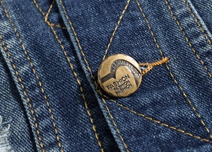 Detailed macro view of vintage bronze button with engraved text on blue denim vest