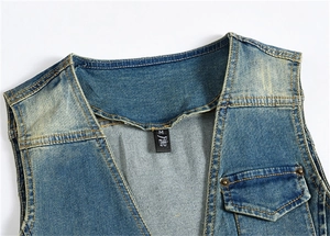 Détail du gilet en jean bleu avec col en V, finition délavée et rivets métalliques cuivrés