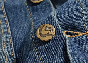 Macro shot of bronze vintage button and yellow contrast stitching on blue denim vest