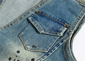 Détail de gilet en jean bleu avec poche bouclier, coutures jaunes et taches de peinture
