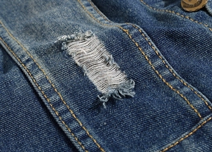 Macro detail of distressed blue denim fabric with vintage brass button and frayed edges