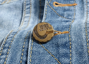 Macro shot of retro metal button with Fashion engraving on light blue denim vest