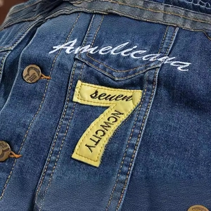 Slim fit blue denim vest featuring white cursive embroidery and yellow patch number seven