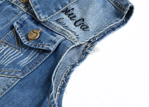 Detailed view of blue washed denim vest featuring embroidery and vintage metal buttons