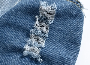 Detailed macro view of distressed light blue denim fabric with ripped holes and fringe