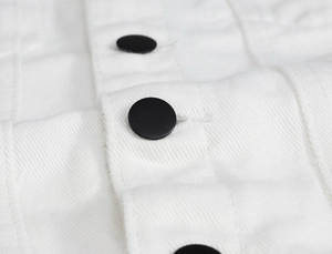 Close-up of black button and stitching detail on a white denim vest for men