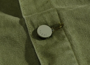Macro shot of olive green denim jacket fabric texture and a metallic button with jeans text