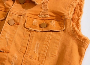 Détail du gilet en jean orange avec des effets usés et des boutons en métal vintage