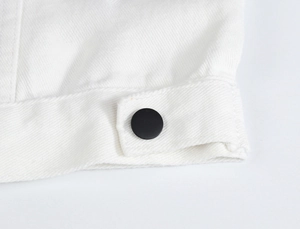 Detail of white denim vest hem featuring adjustable side tab and matte black button