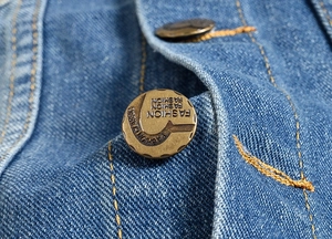 Detail of copper button with Fashion Classic engraving on blue denim vest