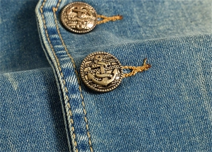Détail d'un gilet en jean bleu avec boutons en métal ancrés et surpiqûres contrastées