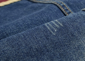 Close-up of blue denim vest fabric with yellow double stitching and worn-out details