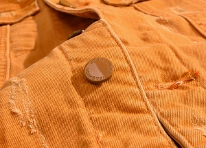 Gros plan sur un gilet en jean orange avec boutons gravés et détails de tissu délavé usé
