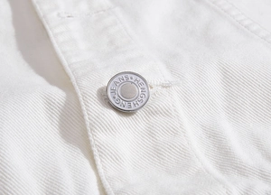 Detailansicht des silbernen Metallknopfes und der schweren weißen Twill-Denim-Textur