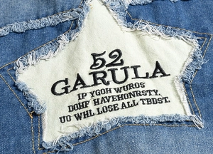 Detail of denim vest featuring star patch with black embroidery and frayed edges