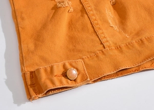 Détail de l'ourlet de la veste en jean orange avec texture usée et bouton en métal mode