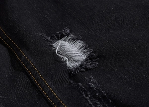 Macro detail of black denim fabric featuring distressed rips and yellow contrast stitching
