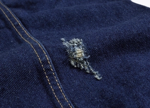 Macro shot of dark blue denim fabric with vintage distressed rip and contrast stitching