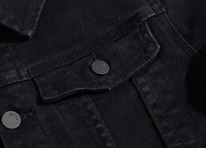 Detail of chest flap pocket on black denim jacket with matte metal buttons and jeans engraving