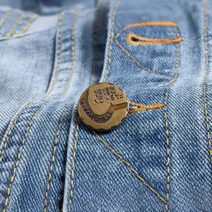 Close-up of a vintage bronze fashion button on light blue distressed denim vest