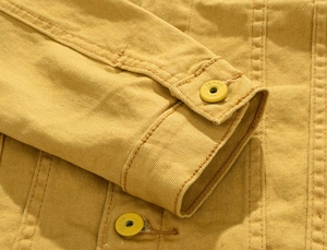 Detailed macro view of yellow denim jacket cuff with branded metal button and stitching